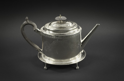 A silver teapot with a square-like body, a half-heart shaped handle, and a straight, narrow spout. It has small feet that end in rounded balls.
