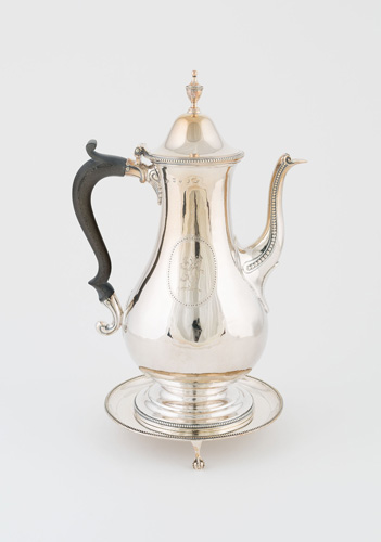 A bright silver pot-belly coffee pot with a darker black or brown handle. It is decorated with small beads of silver around the edge of the lid and the side of the curved spout, and has an etching of a rearing lion. The pot rests on a tray with a small foot that ends in a silver ball.