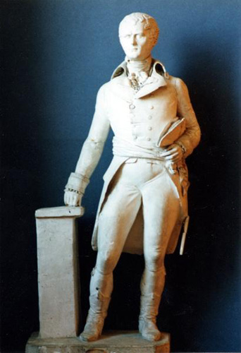 An all-white sculpture of a man standing with his weight on one leg, leaning one hand against a pillar. He wears a sash belt, a coat with a high collar and long tail, and may have a folded hat tucked into his arm.