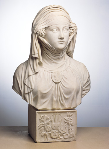 A grayish-white bust of the head and chest of a woman, set on a square base decorated with flowers. The woman wears a wrapped and draped cloth that covers her neck, head, and forehead, leaving only a small portion of her face from teh eyebrows to the chin visible. Part of her braided hair pokes out of the wrap at ear level.