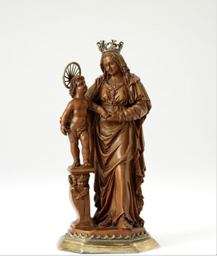 A medium brown-colored carving of a woman in a draping dress with a large crown on her veiled head, holding a nude infant with a halo who stands on a pedestal by her side. The child looks up at the woman, who gazes downward.