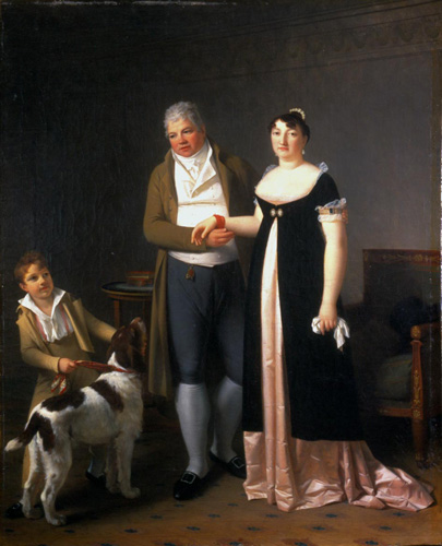 A man and a woman stand at the center of a room, with the man holding the woman's arm. the man has gray hair, light skin with rosy cheeks, and  a long green coat over a white waistcoat with a high collar, and he is looking down and away from the woman next to him. The woman has very light skin, dark curly hair pulled away from her face, and wears a short-sleeved black and pink dress. On the other side of the man, a young boy in a green coat is holding a white and brown spotted hunting dog by the leash.
