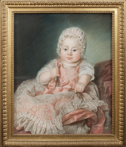 A light-skinned infant with pink cheeks and dark eyes is dressed in pink with white lace.