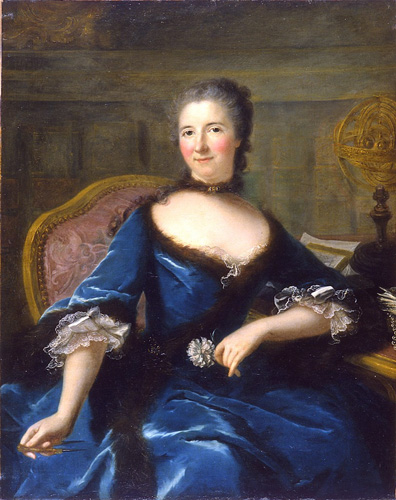 A woman with very light skin, very pink cheeks, and long dark hair that is gray at the roots is seated at a table, looking out at the viewer. She wears a royal blue dress with brown or black fur trim and white lace at the ends of the sleeves, a short choker-like necklace around her neck, and holds a flower in one hand. In her other hand, she holds what may be a pen or pencil.