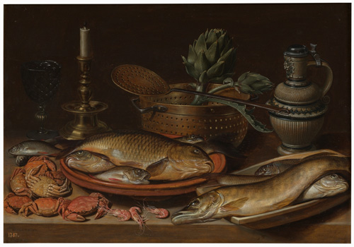 A table is spread with two platters of whole fish, some big and some small, with a few shrimps on the table in front of the platters and five or six small crabs off to one side. Behind teh seafood, a whole artichoke is in a metal colander next to an unlit candle and a jug.