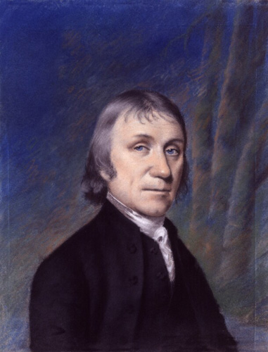 A light-skinned man with thin lips, thin gray hair, and bright blue eyes is shown from the chest up. He wears a black coat with a tall white collar.