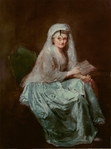 A woman with light skin, gray hair, and a lined face is seated, leaning forward with a book in her hand. She is turned to look at the viewer, and has a monocle affixed to her head in front of one eye. She is wearing a pale blue skirt with an off-white or gray shirt or shawl and a veil over her hair.