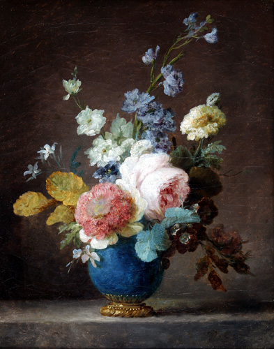 A blue vase of flowers is shown with a small flower arrangement. The central flowers are pale pinks and white, with other flowers that are yellow, light blue, or purple.