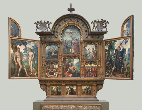 A large, carved wooden altarpiece with two doors swung open has thirteen small paintings inside. On the left door, a light-skinned nude man and nude woman stand in a garden, holding an apple between them. In the center, six images depict a group of light-skinned people kneeling over an infant child; a group of light-skinned people, mostly women, kneeling over the emaciated body of a brown-haired, light-skinned man, with a wooden cross in the background; a large central image of a light-skinned brown-haired man wearing only a loincloth suspended from a wooden cross by his hands and feet, with three women gathered at the bottom of the cross; an aged, light-skinned nude man with a bald head and gray beard kneeling on the ground with a blue cloth and red cloth, the man on the cross visible behind him; a light-skinned man with brown hair standing in a river with his hands clasped, while another man with similar features stands on the shore holding his hands over the man in the river's head; and a large group of people kneeling, raising their hands up, and looking toward the sky, where above their heads, a pair of feet is just visible in the air above them. Finally, on the right side door, a young boy with light skind and red hair kneels at the feet of an older man with light skin, a gray beard, and a red cap, who has his sword raised over his head to strike, while far above a golden-haired, light-skinned angel in white robes holds back the sword.