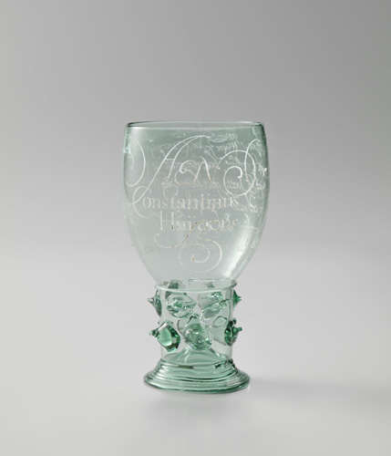 A glass goblet with spike-like glass projectections from the short stem. The bowl of the glass is etched with words in an ornate, swirling script.