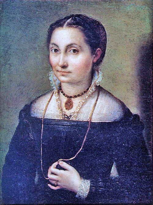 A portrait of a young woman looking directly at the viewer with a slight smile. The composition is cropped at her waist, and she is holding her necklace in her left hand. She is elegantly dressed in sixteenth-century clothing.