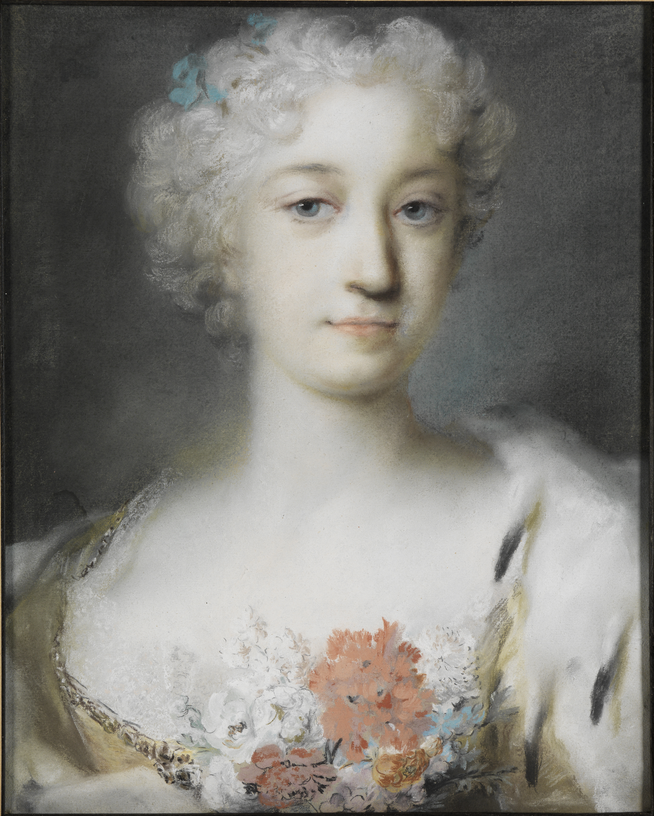 A bust-length portrait of a young woman wearing an eighteenth-century white wig with blue bows. She is elegantly dressed, with a spray of flowers at her bust. She looks directly out at the viewer. 