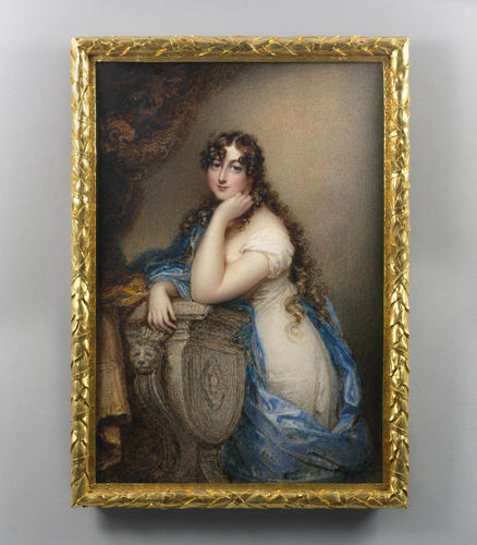 A rectangular, three-quarters length portrait in a gold frame. The young woman is wearing a white gown with blue fabric draped across her. She is leaning on a pedestal or table, with one elbow propped up and her chin in her hand. Curls frame her face, and her waist-length hair is loose in the back. The background is a neutral brown-gray color, with a curtain tied back on the left side.