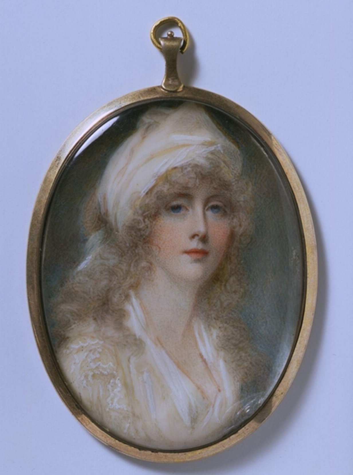 An oval portrait miniature of the artist wearing a white dress with a white scarf tied in her hair. Curls frame her face and fall around her shoulders. She looks out directly at the viewer with a confident, neutral expression. She has intense blue eyes and coral cheeks and lips.