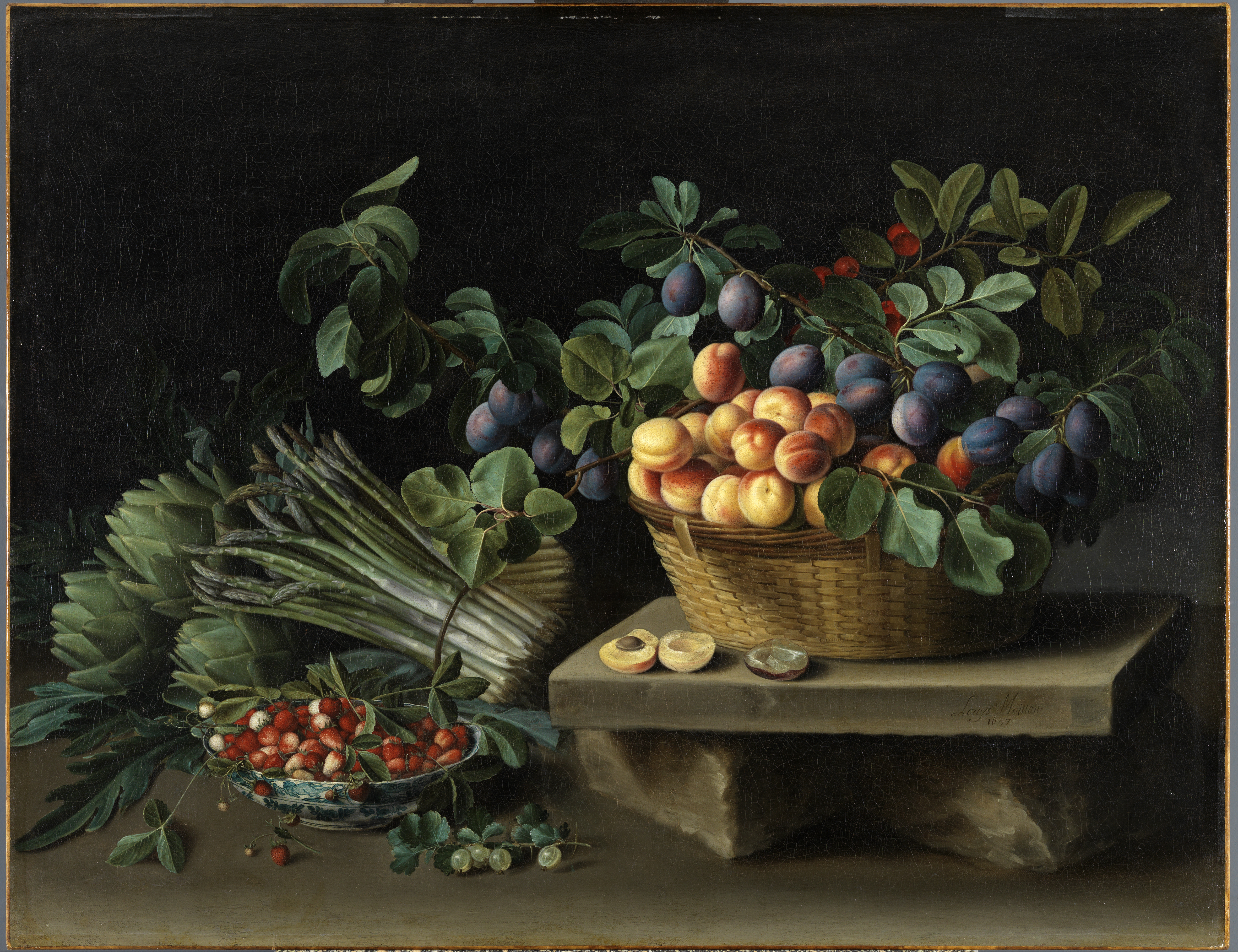 Fruits and vegetables are arranged on a simple table against a black background. On a slab of rock, there is a basket of plums, peaches, and other small fruits. To its left, there is a smaller white and blue porcelain bowl of strawberries. Just behind that bowl, there are bunches of asparagus tied with brown cord and artichokes. It is a lush scene, with green foliage adorning the various arrangements.  