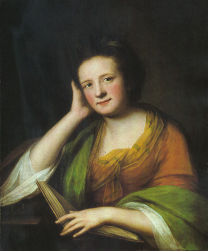 A half-length portrait of a woman looking up from her book to meet the viewer’s gaze directly. One hand holds the book while she rests her head in the other, her elbow propped on a table. She is wearing an orange and marigold gown, with a green shawl draper around her. Her hair is pulled back to show her rosy cheeks and her expression is a slight smile. 