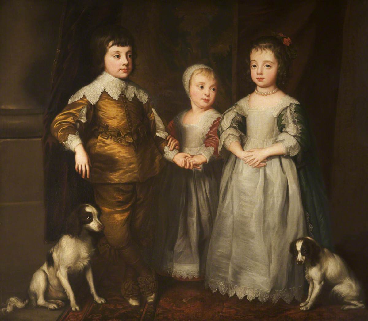 A full-length portrait of three children, two girls and a boy. The boy is wearing a bronze-colored outfit with lace trim and the girls are wearing gray dresses with lace trim and other embellishments. The older girl has her curls pulled half-back while the young girl wears a lace cap. There are two white and brown dogs seated on either side of the group and the younger girl is holding the hand and arm of the boy.