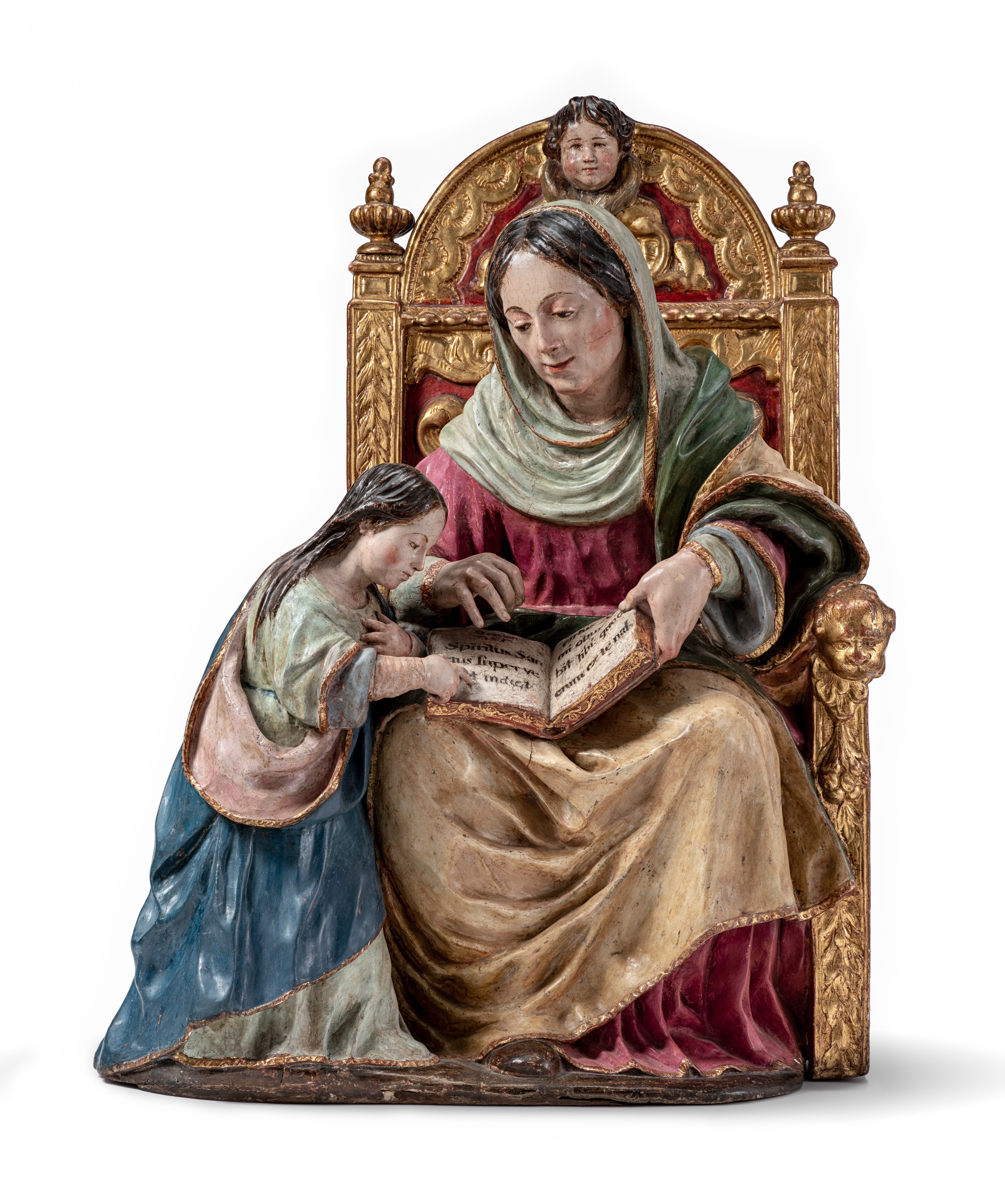 A polychrome wood sculpture of a woman seated in a red and gold throne, wearing classical or Biblical robes, with a book open in her lap. Beside her, a young girl who is also dresses in robes stands and points to the book, looking intently at the page. The woman also gestures at the page, engaged in conversation with the young girl. The crown is adorned with the face of a child at the top.