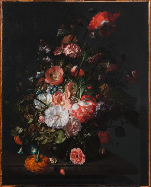 A floral still life of an arrangement on a table, set against a dark neutral background. The colors of the flowers are primarily reds, oranges, and purples, with some large white flowers at the center. The arrangement is wild, with flowers resting on the table and extending to the very top of the composition.